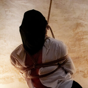 une personne en chemise blanche et un sac en tissus noir est attaché par des cordes de shibari