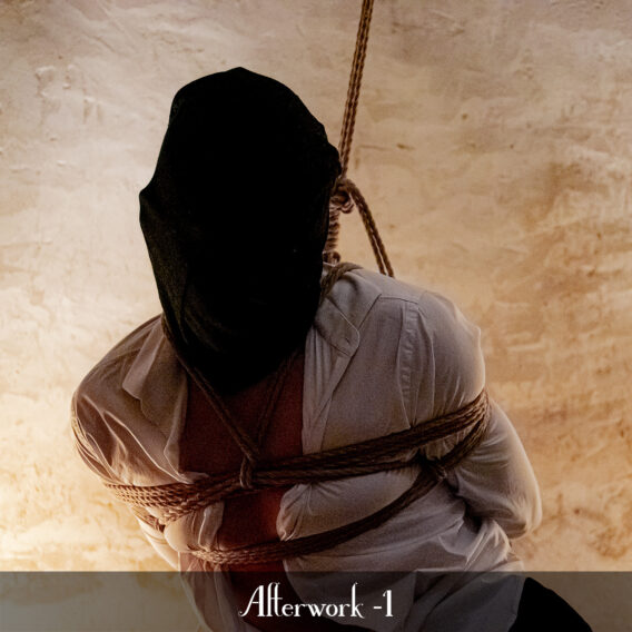 Un homme en chemise blanche et la tête recouverte d'un sac noir est attaché dans une cave par un bondage shibari.