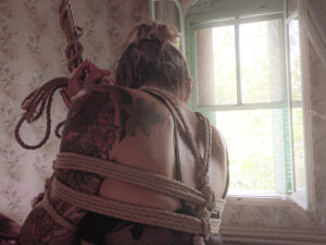 Une jeune femme est attaché par des cordes de shibari dans une immense maison abandonné, un halo de soleil la réchauffe.